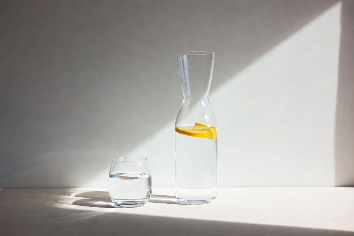 Carafe d'eau et verre sur table en bois évoquant l'hydratation quotidienne et le confort urinaire de la prostate Carafe d'eau et verre sur table en bois évoquant l'hydratation quotidienne et le confort urinaire de la prostate