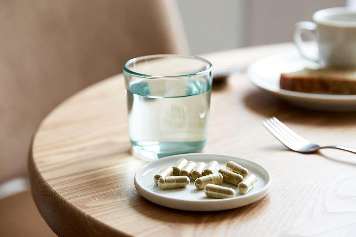 Prise du Permixon au repas pour réduire chaque effet secondaire digestif : gélules et verre d'eau sur une table Prise du Permixon au repas pour réduire chaque effet secondaire digestif : gélules et verre d'eau sur une table
