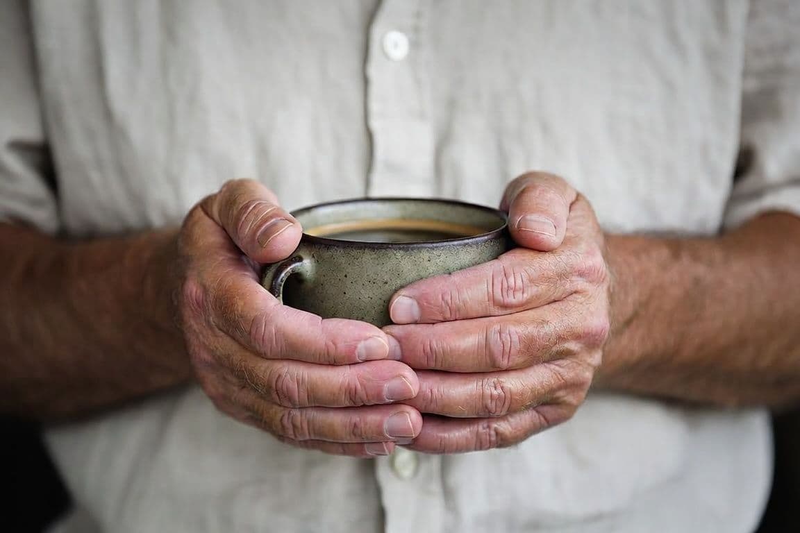 Mains d'homme mature tenant une tasse de café matinal évoquant la fatigue liée à l'hypertrophie de la prostate Mains d'homme mature tenant une tasse de café matinal évoquant la fatigue liée à l'hypertrophie de la prostate